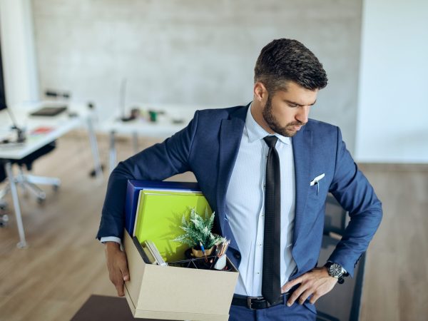 Distraught businessman holding his belongings and feeling worried while getting fired from his job.