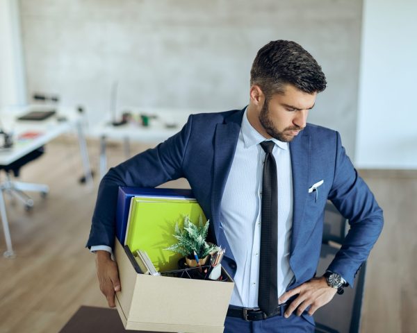 Distraught businessman holding his belongings and feeling worried while getting fired from his job.